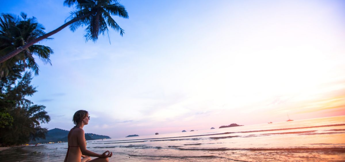 Young woman practicing yoga on the beach at sunset.